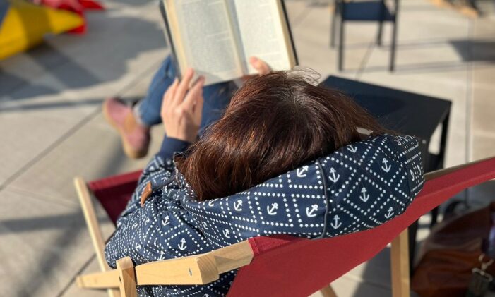 žena sedící v plátěném lehátku na terase, čtoucí si knihu